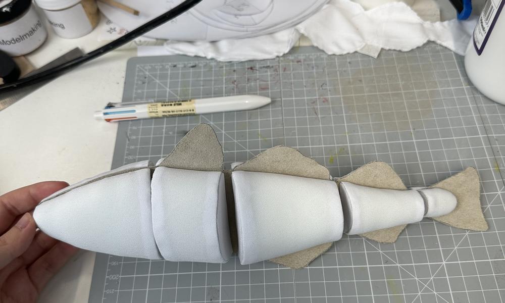 Early stages of making a model cod, showing the body and fins made from soft textile material, grey drawing board surface.