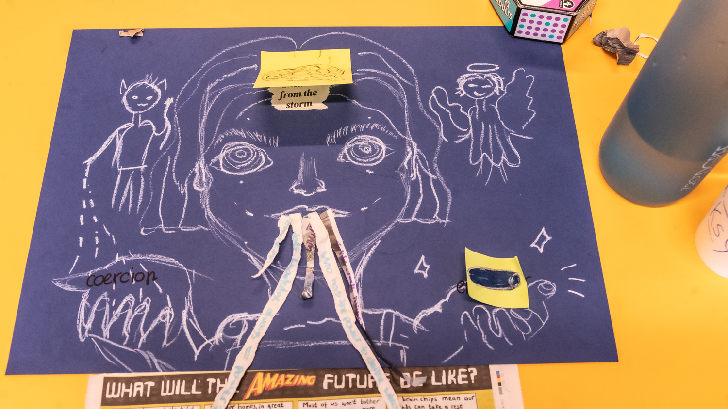 Purple paper with white chalk drawings of face, stick figures, and objects. Yellow surface underneath. Person's hands visible at bottom centre.