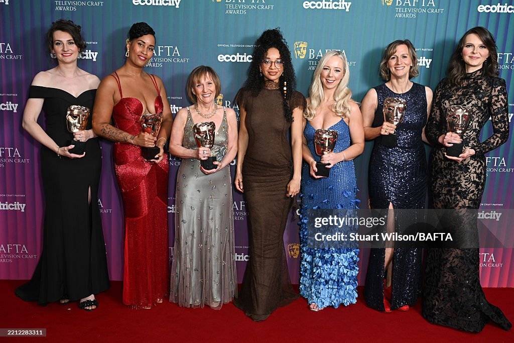 Seven women in formal gowns holding BAFTA awards on red carpet. Dresses in black, red, silver, brown, blue, and patterned fabrics.