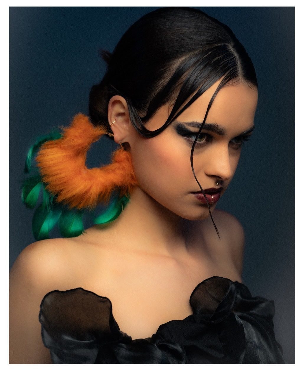 A model wearing an orange/green feathered earring taken on film.