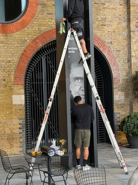 Ladder in front of black pillar showing Andy Earl's work, brick arch in the background.