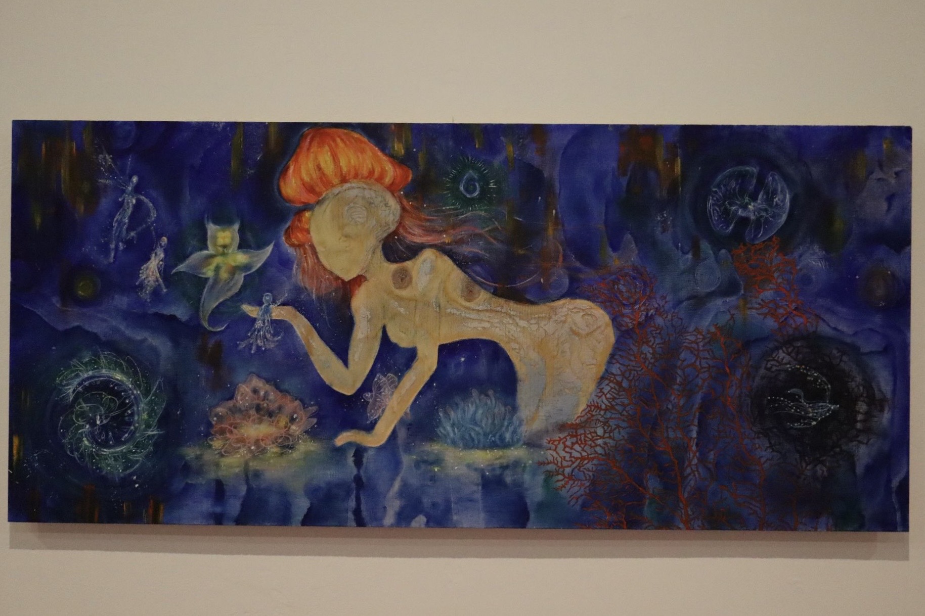 A long rectangular painting shows a nude red-haired figure underwater, surrounded by blue-purple abstract swirls and small sea-like shapes on a beige wall.