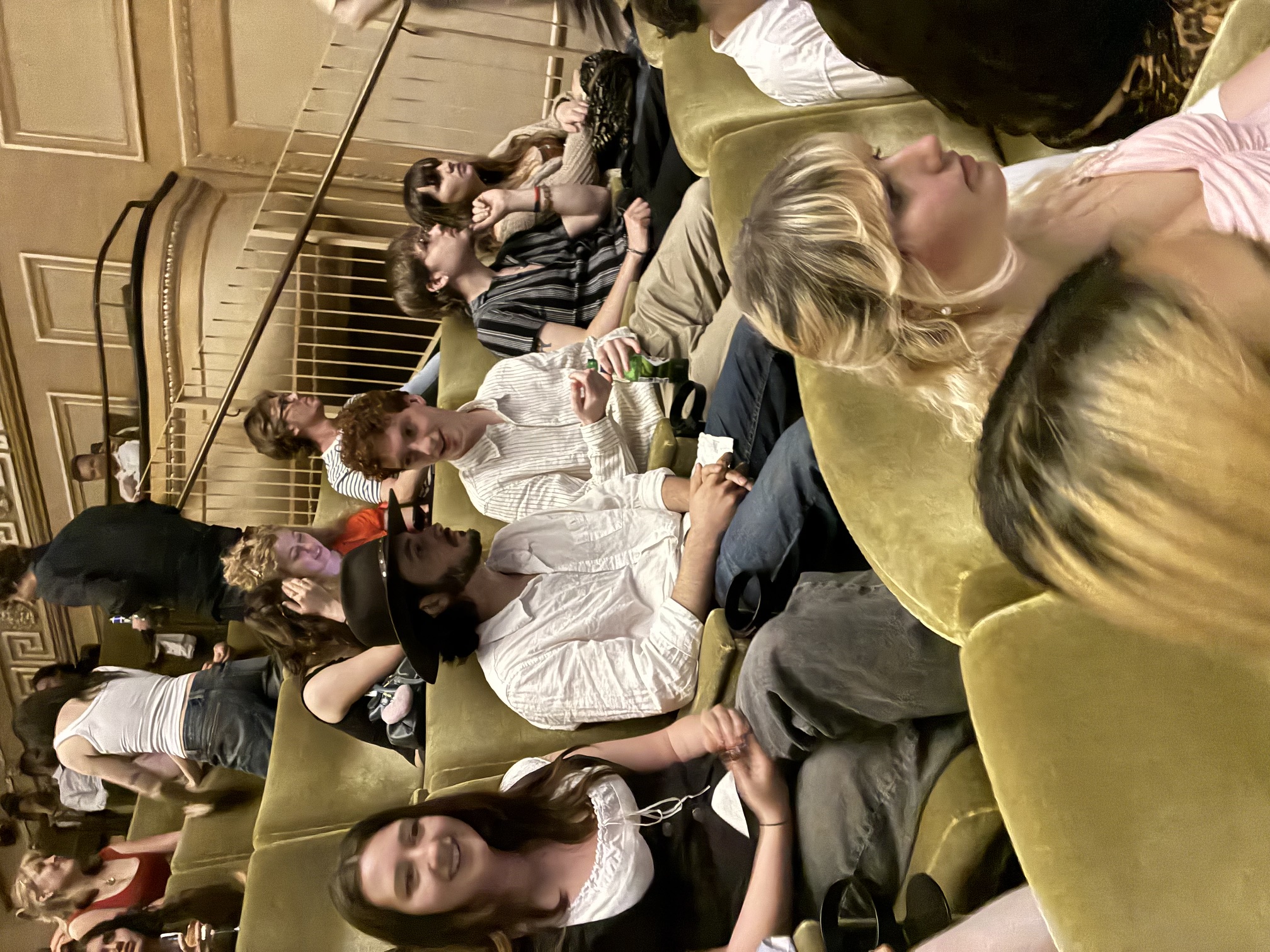 People sat in green chairs talking, stairs and beige wall panelling in the background.