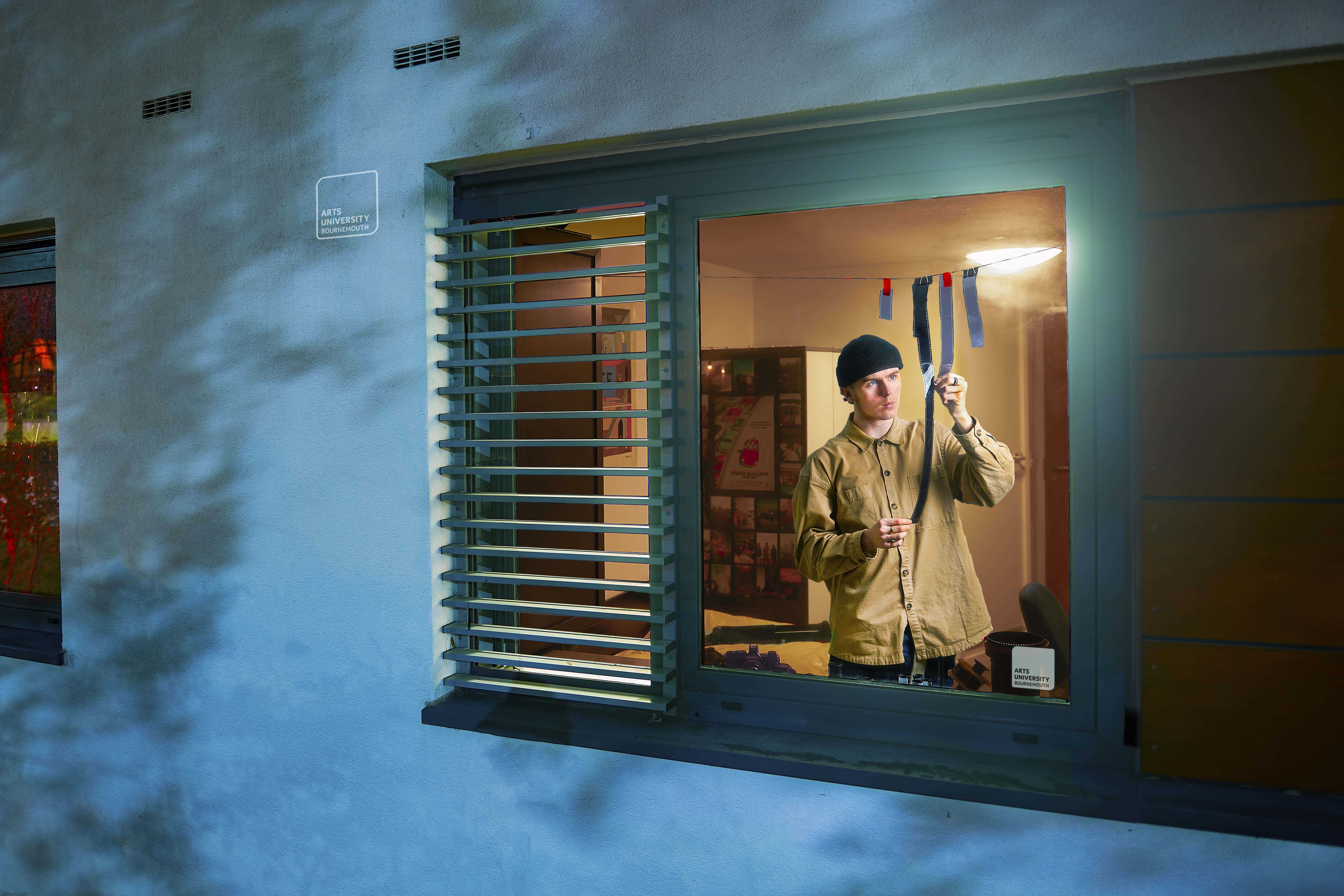A person stands at an open window and examines strands of camera film