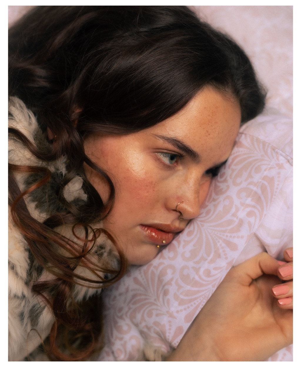 A close-up of a model with blushed cheeks and dark hair upon a punk duvet.