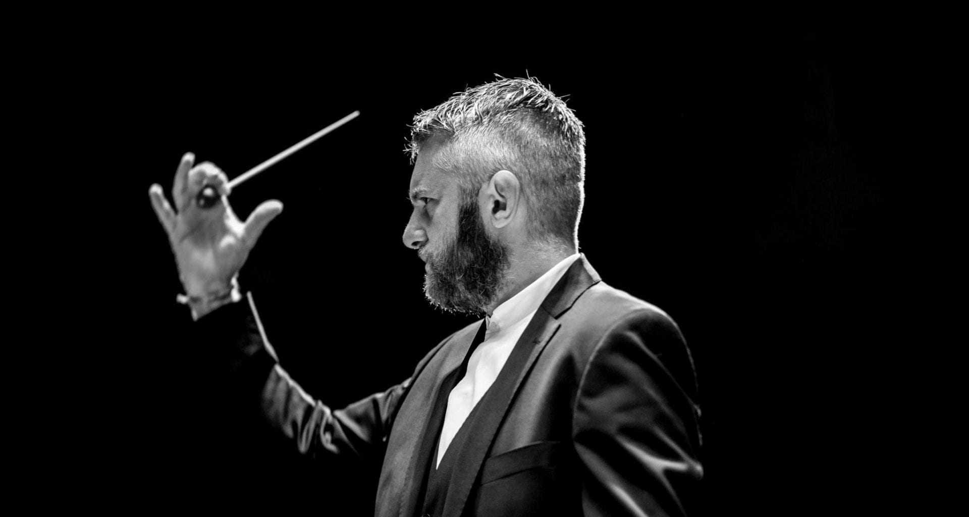 Side view of a conductor with their hand and baton held out in front of their face.