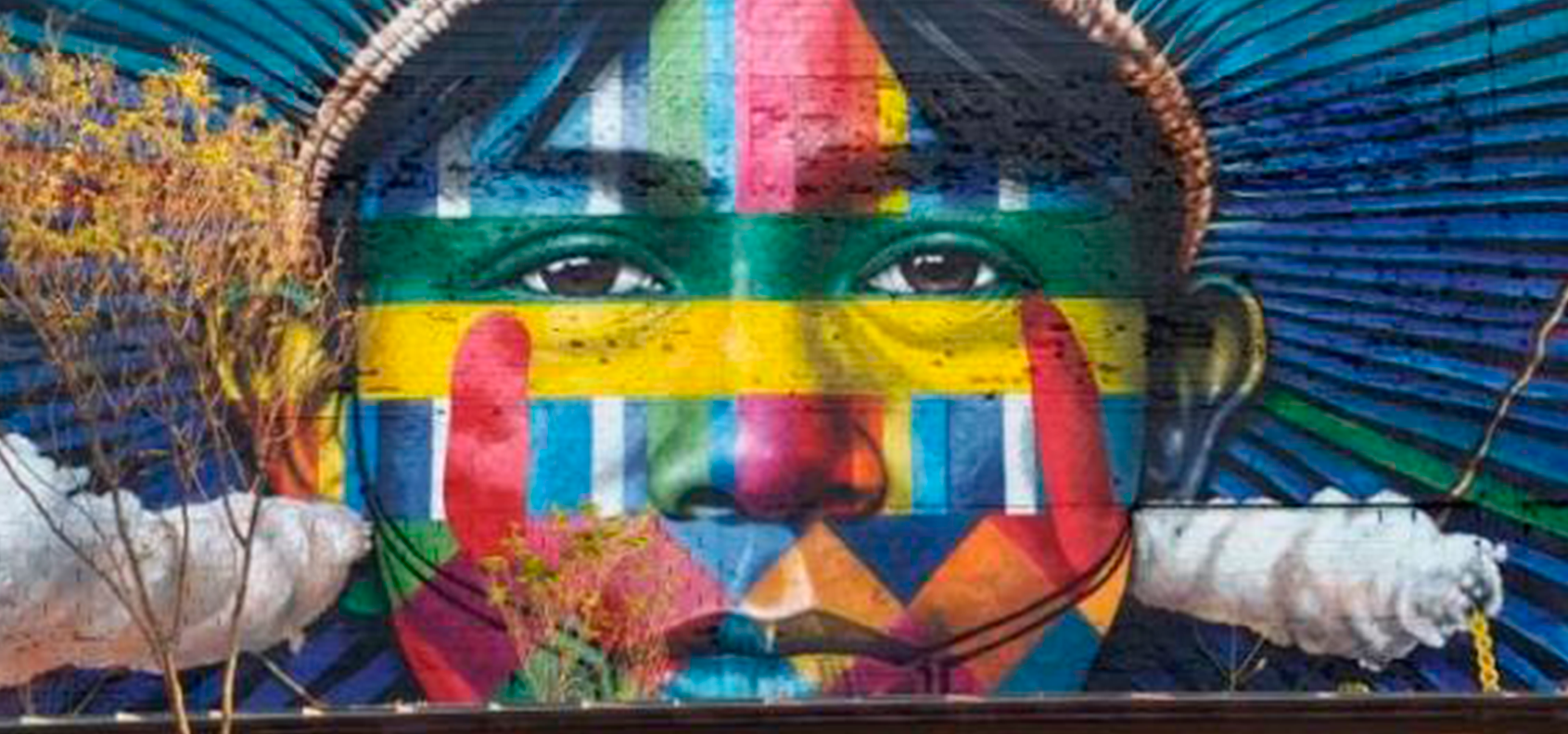Mural of a man's face made up with multiple colours and shapes. Trees and clouds also appear.