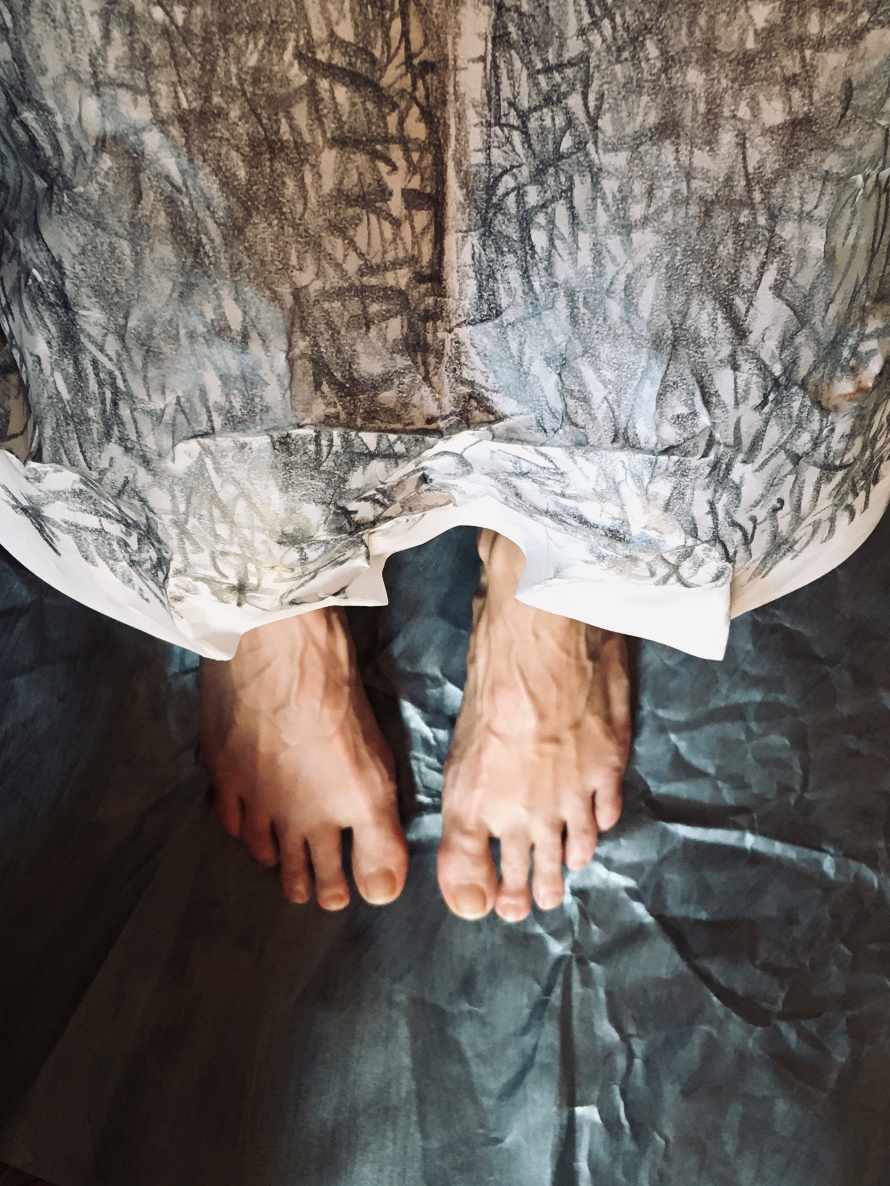 A pair of feet emerge from a big sheet of paper with charcoal marks drawn on it.