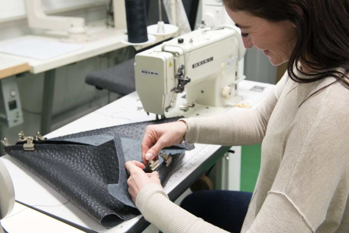 Student folding and clipping a sheet of leather next to a sewing machine