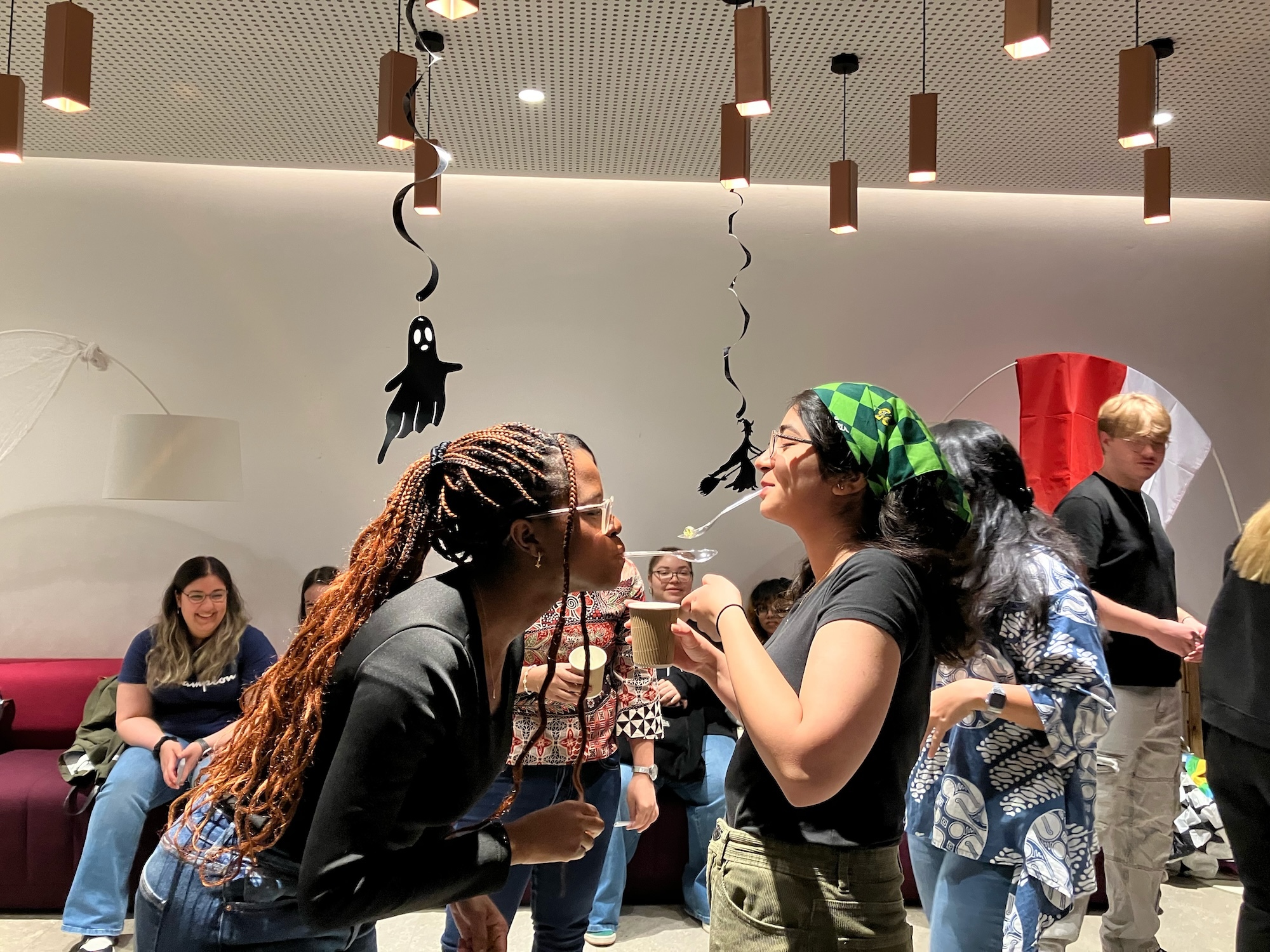 Two Arts University Bournemouth students playing a relay game with marbles in spoons in their mouths at an event at Madeira Road Halls of Residence.