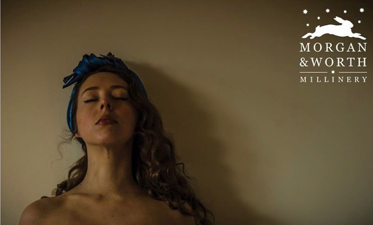 Woman wearing a hair band lies back with their eyes closed and their head against the wall. Logo with the text "Morgan & Worth Millinery" appears in the top-right corner.