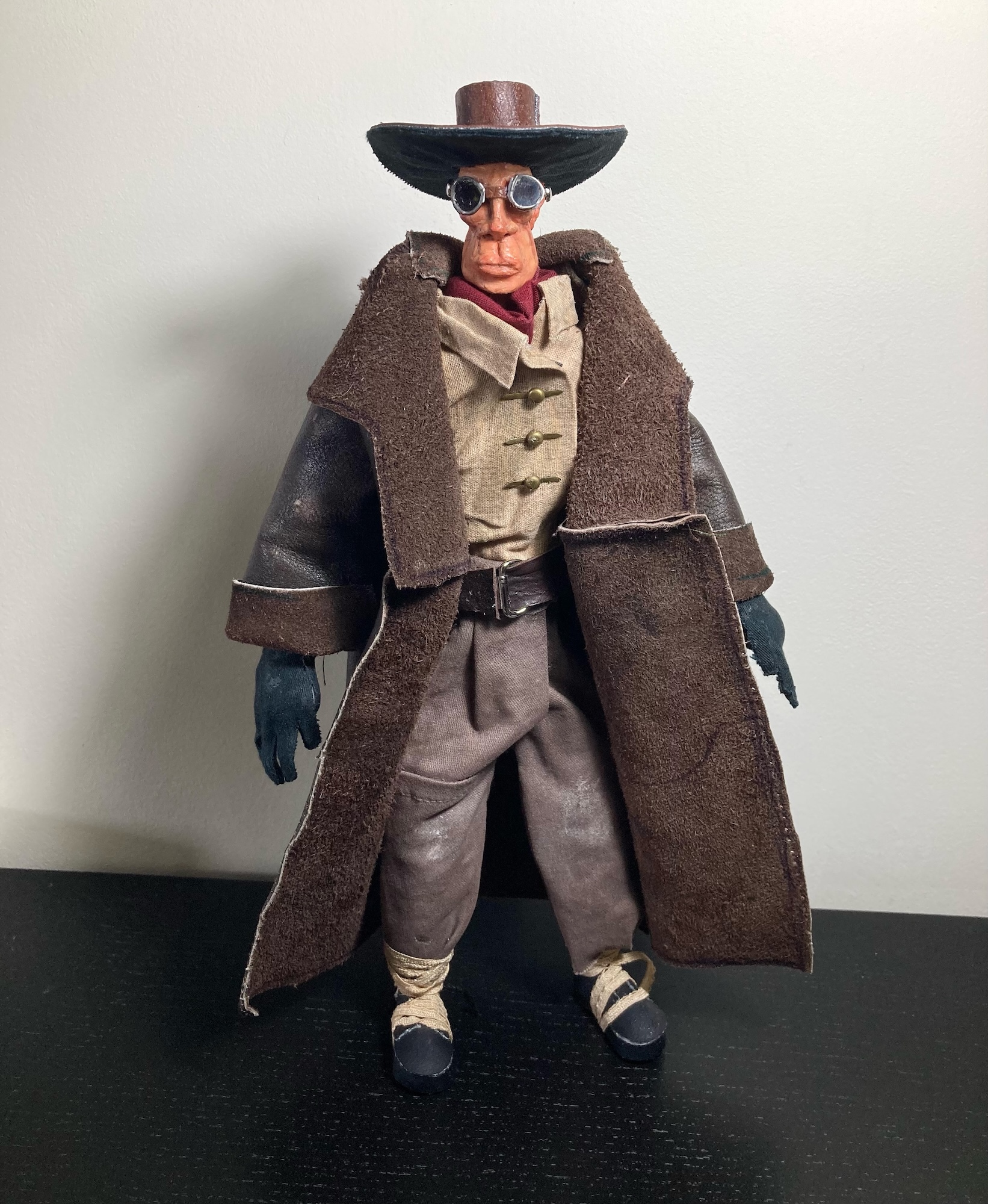 Action figure wearing brown wide-brimmed hat, round glasses, brown long coat, beige waistcoat, and grey trousers against white background.