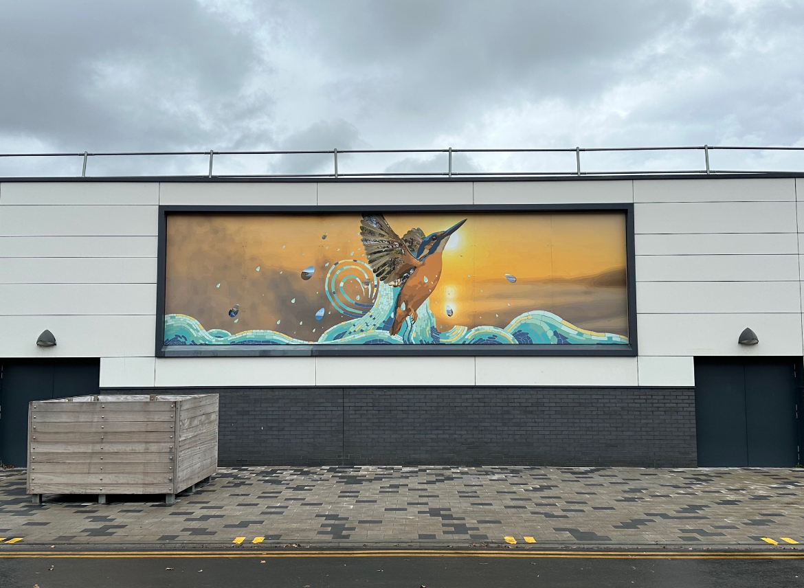 Large mural on grey building facade showing brown bird with spread wings above blue waves against orange-yellow sky background.
