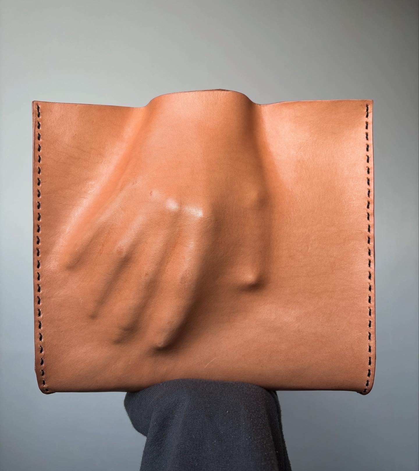 A leather bag or pouch with the shape of a hand embossed onto the side.