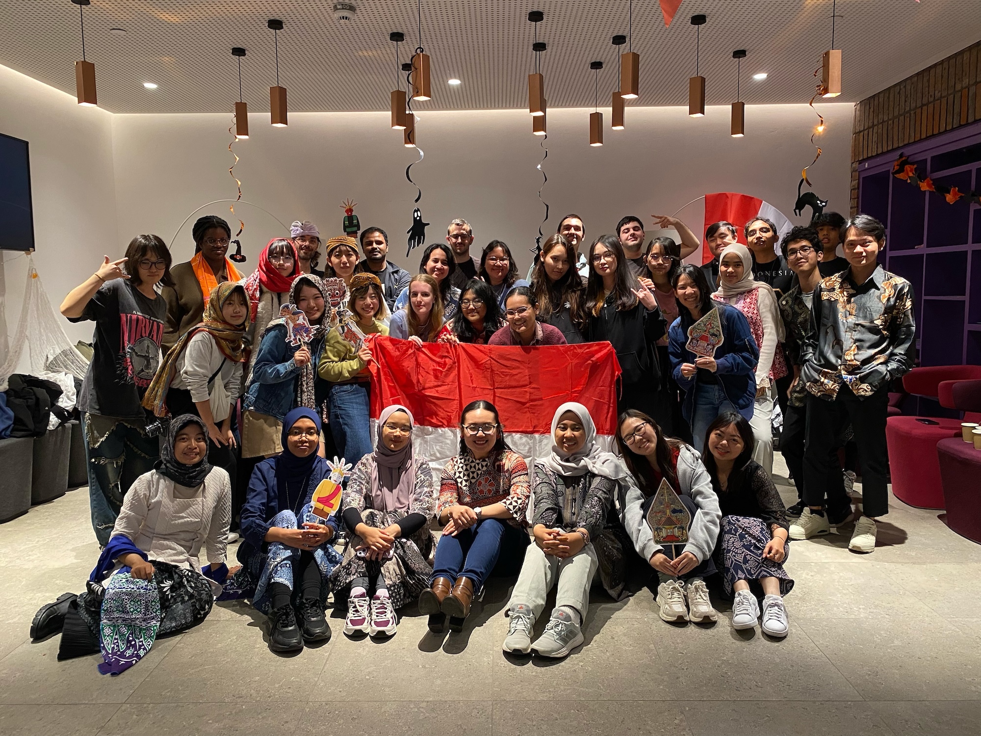 A large group of Arts University Bournemouth students gathered for a photo at an event at Madeira Road Halls of Residence. Some are holding an Indonesian flag in the centre.