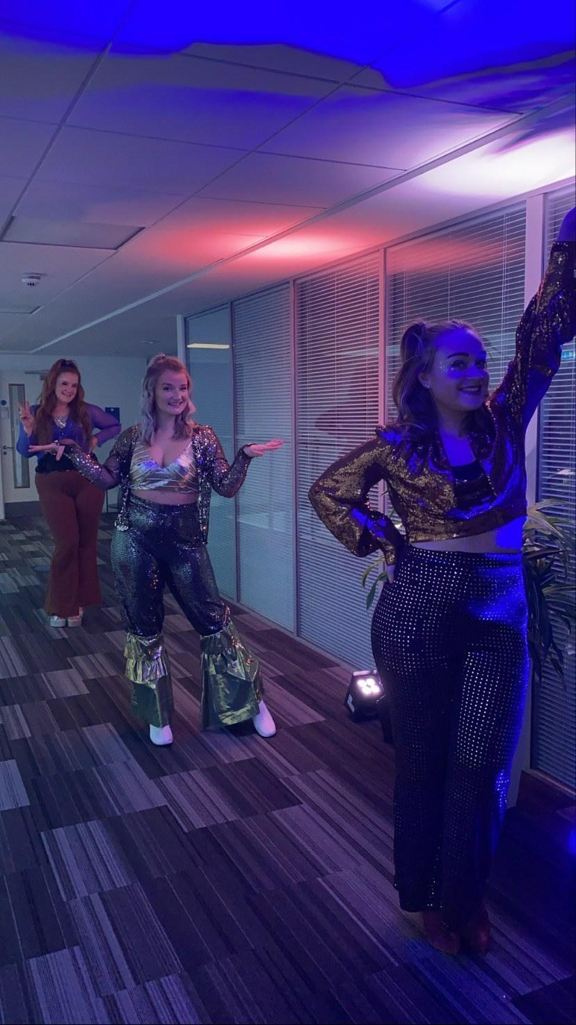 Three dancers in costume perform a routine in a corridor.