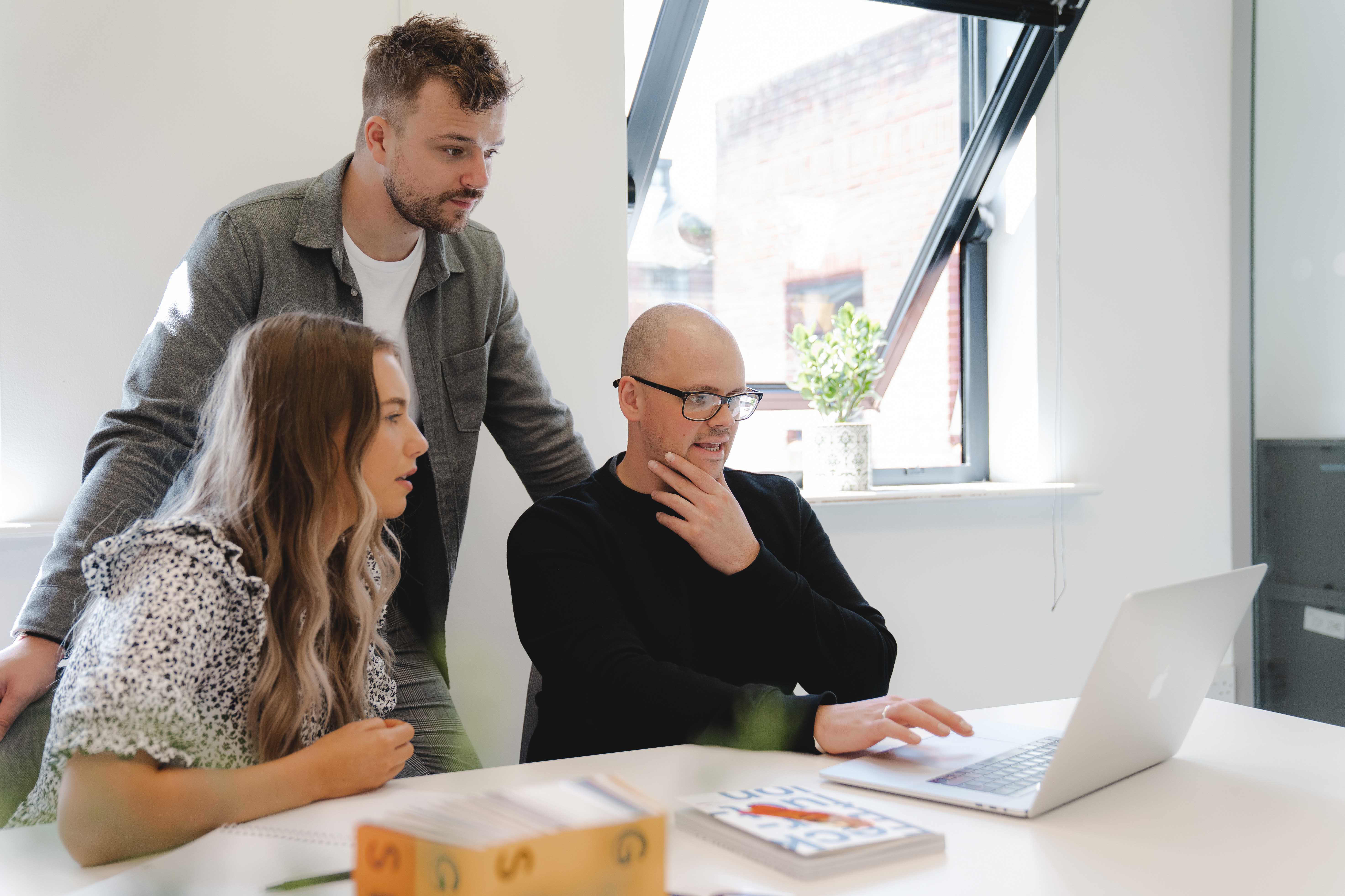 Three people sit at a table and work on a project together on a laptop.