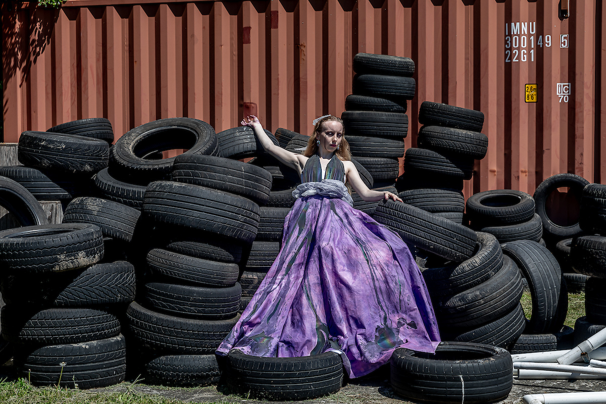 A woman wearing a purple flowing dress on a pile of tyres.