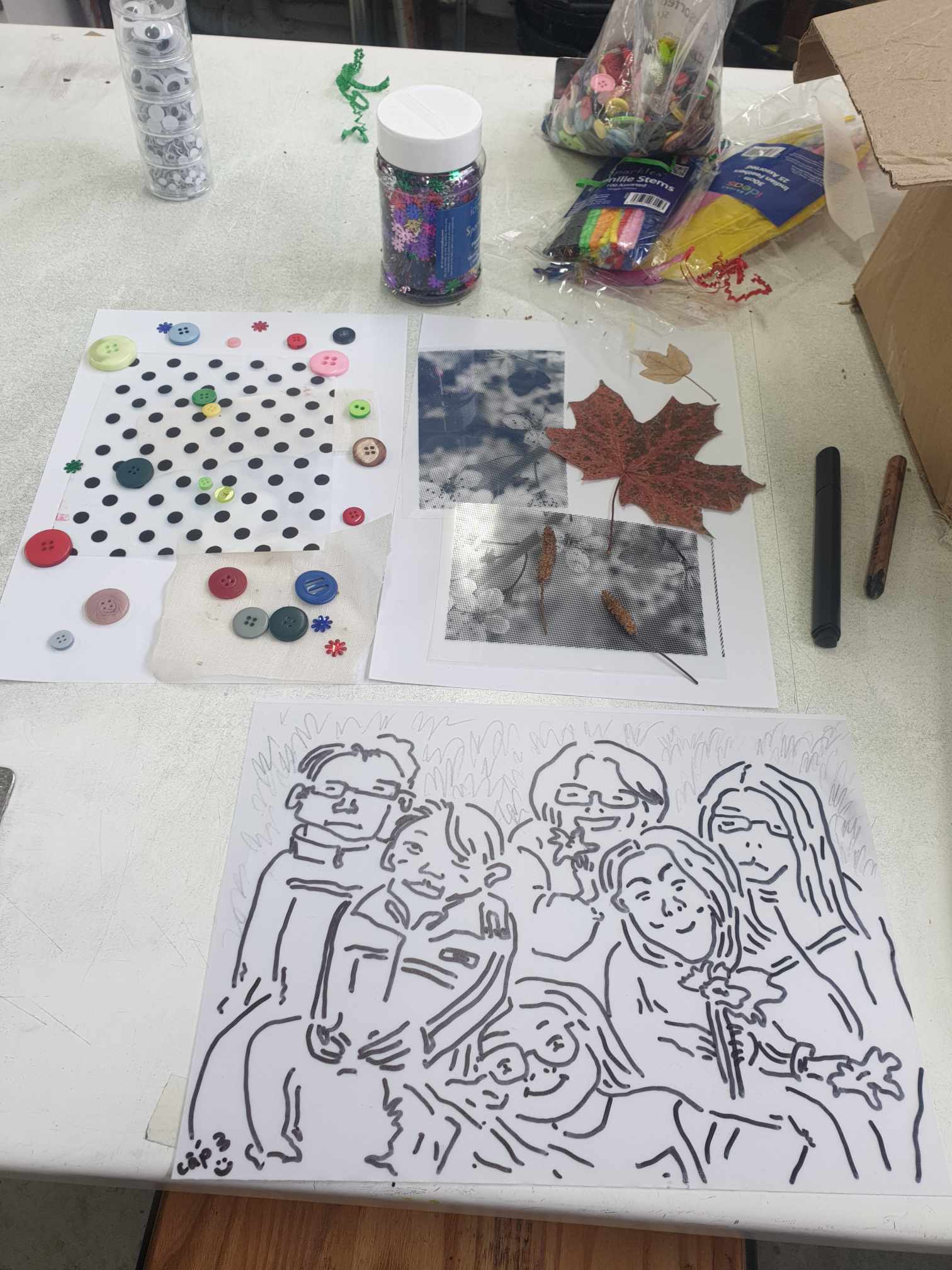 A collage of objects and a printed illustration with outlined people on a table.