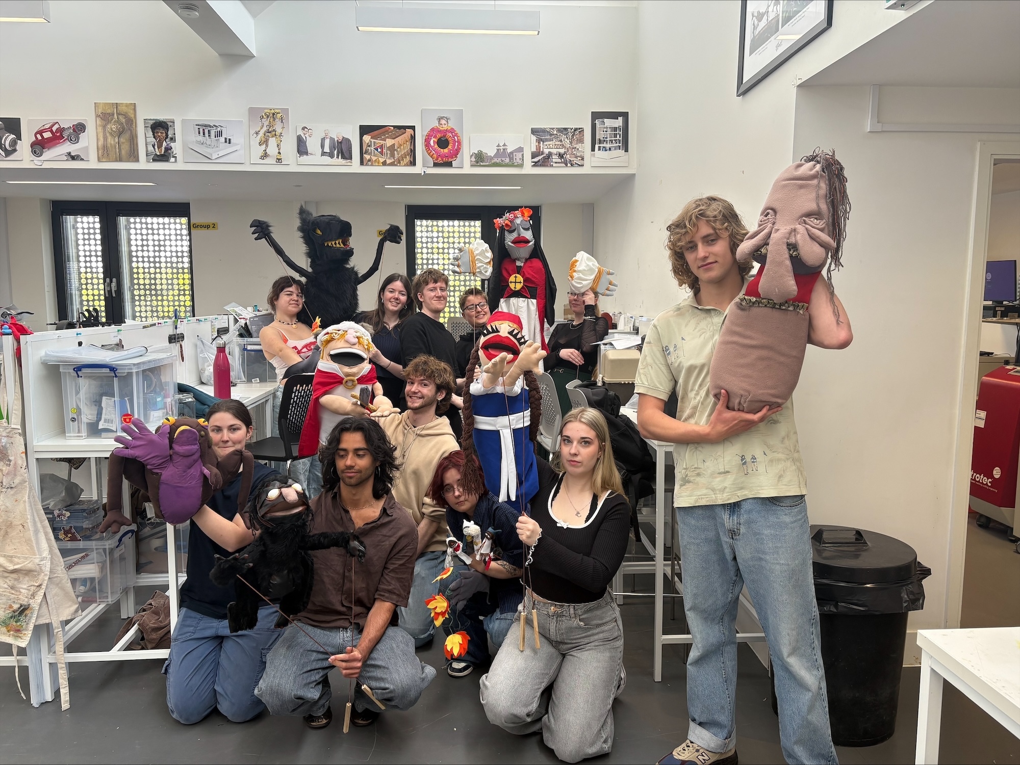 A group of BA (Hons) Modelmaking students pose for a photo holding assorted puppets in a studio space at Arts University Bournemouth.