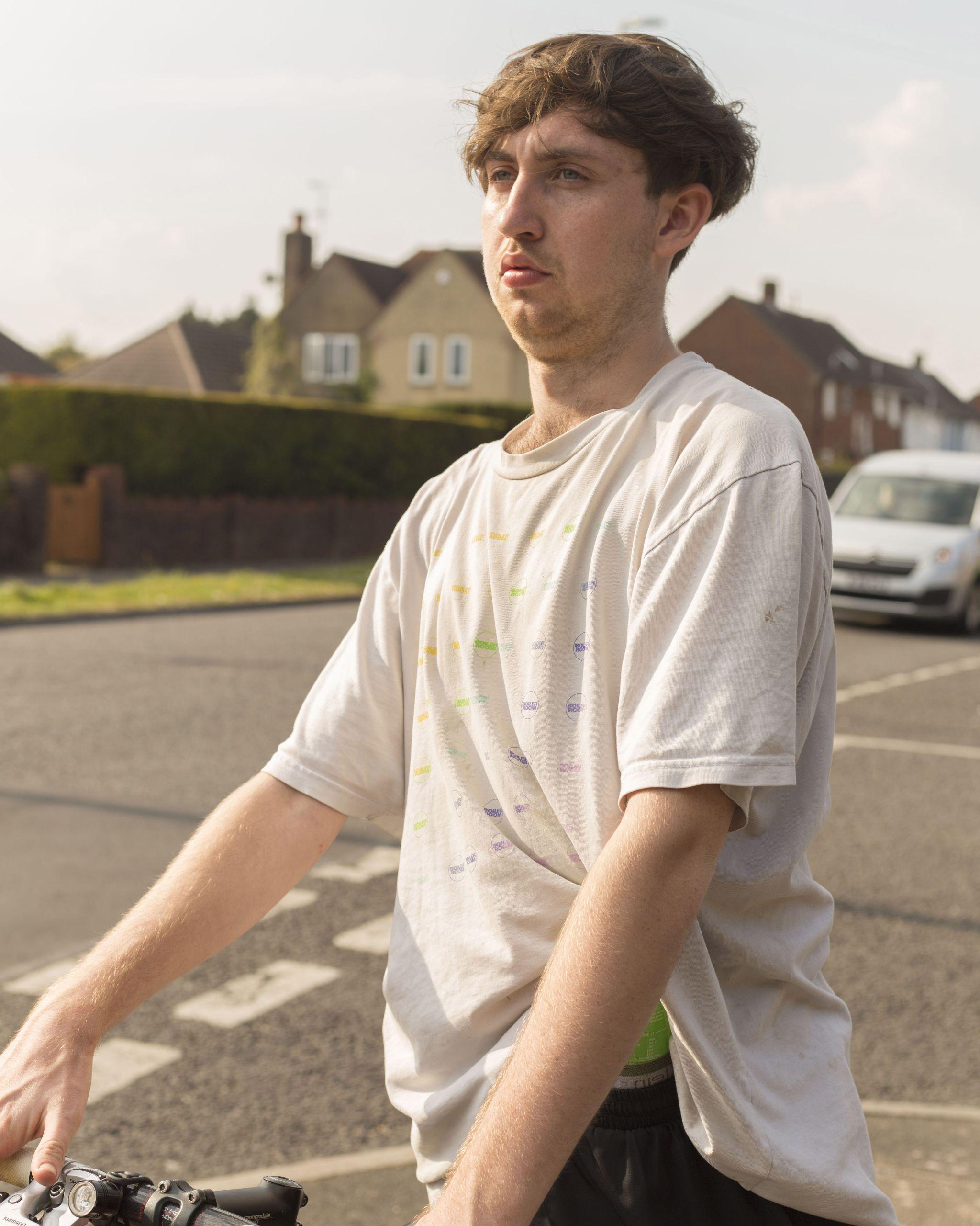 A person stands near a road holding their bicycle.