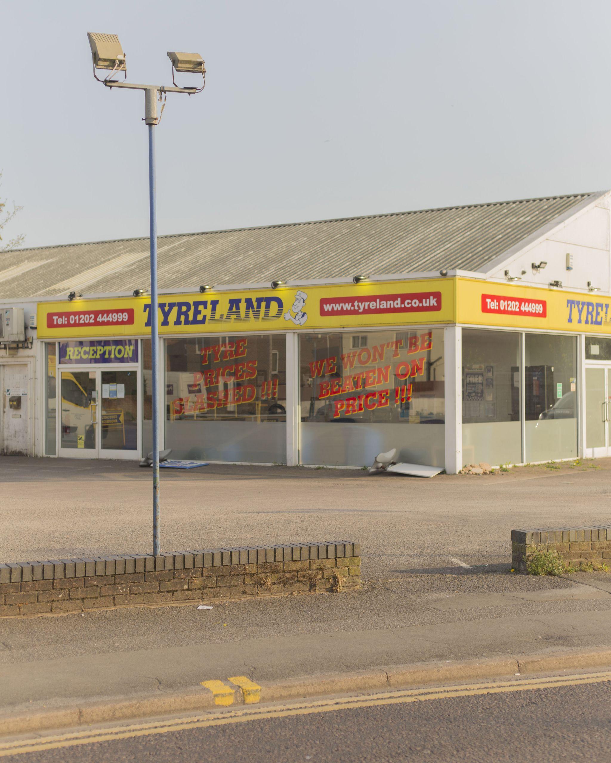 Exterior photo of a Tyreland shop and the surrounding car park and pavement.