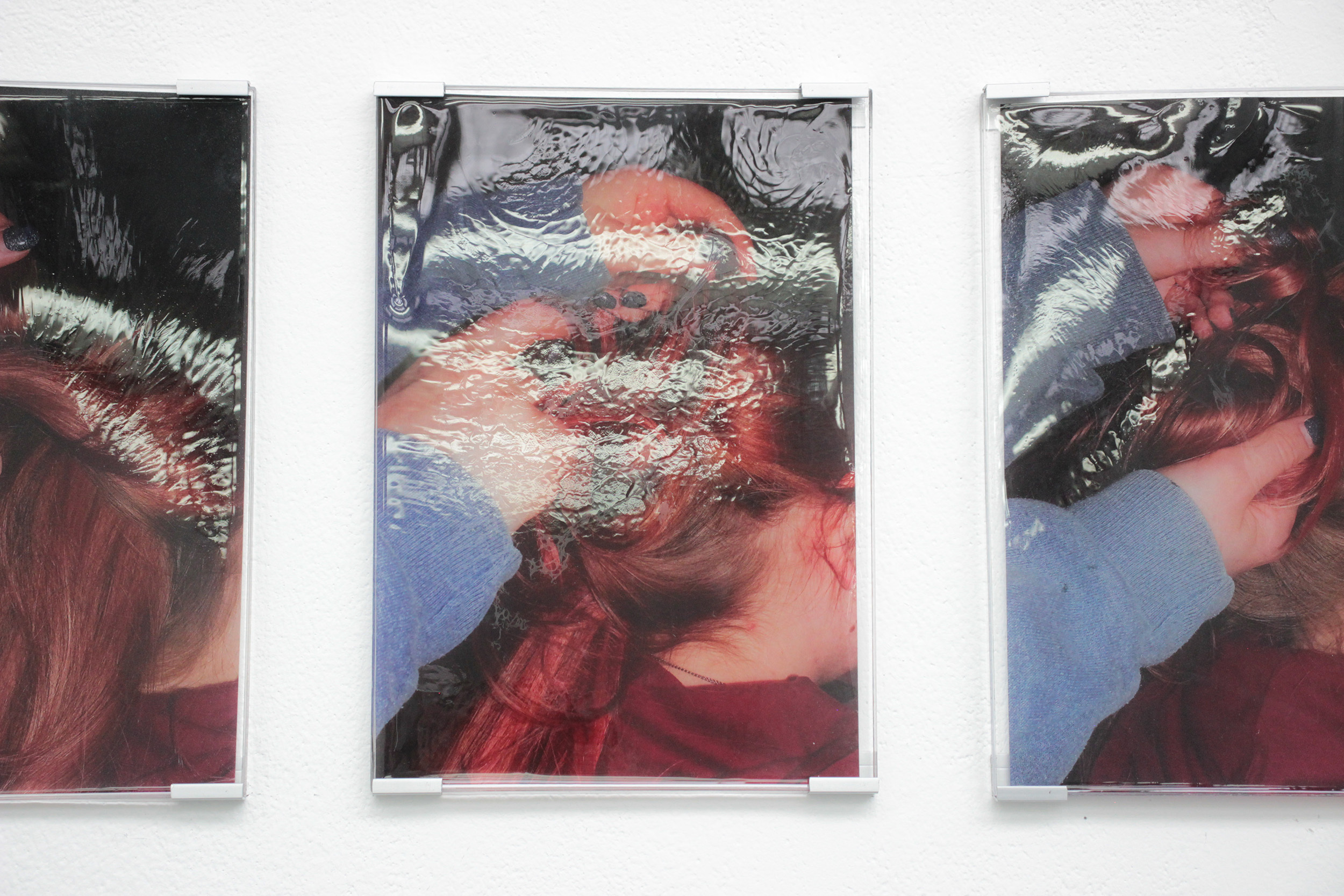 A close-up view of one of the resin plaques depicting the girl wearing blue doing the girl wearing reds hair. There is a gloss over the resin as the light reflects on it, creating movement and partially obstructing the view of the full image.