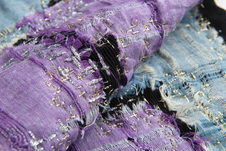 Close-up image of rolls of purple and blue distressed fabrics.