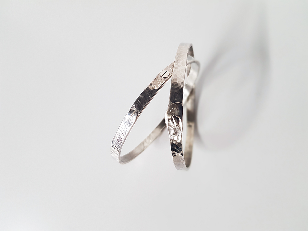 Close-up of two silver rings posed one over the other on a white surface.