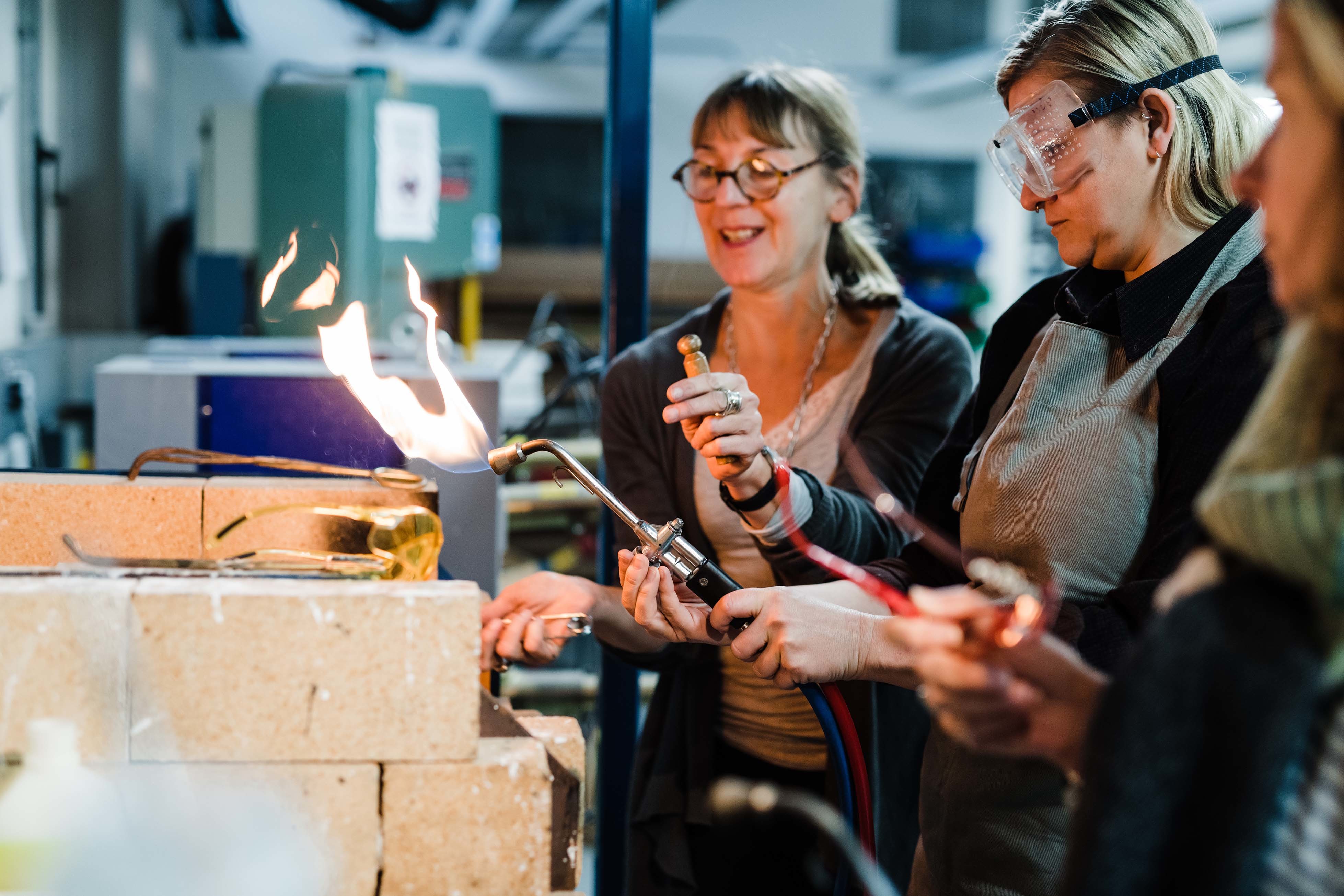 A pair of students stand operating blowtorches.