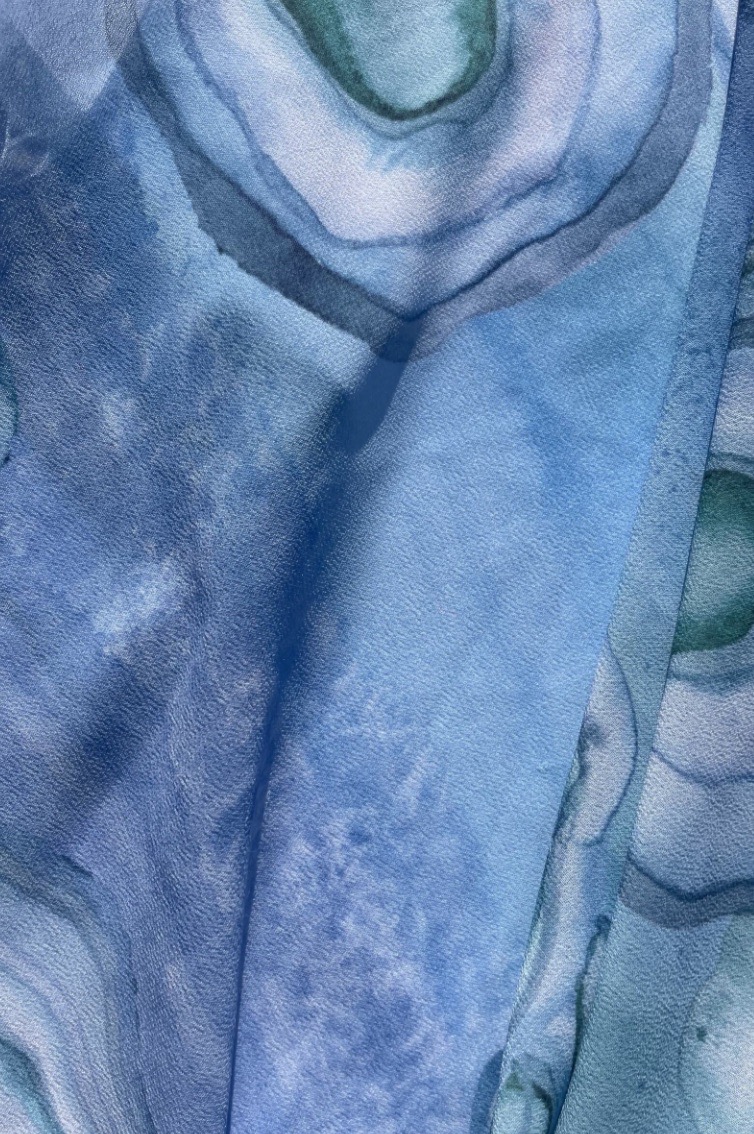 A close-up image of a fabric featuring a blue and green abstract pattern, resembling layers and circular shapes, with various shades of blue and hints of green creating depth and texture.