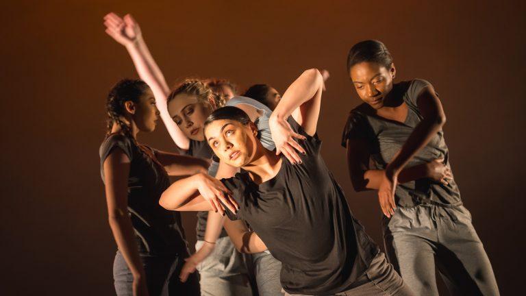 Several dancers in the middle of a routine lean out and pose