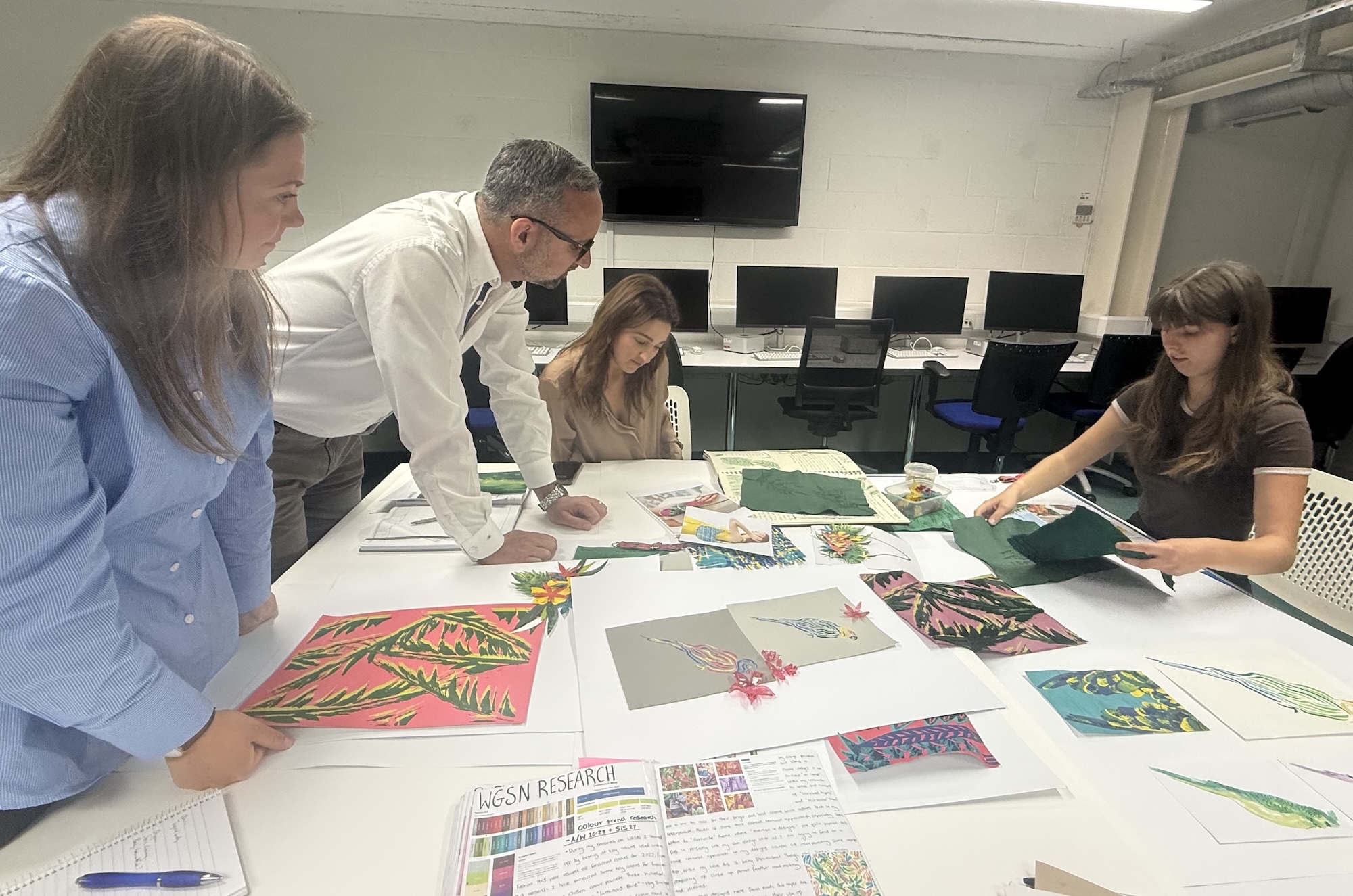 Three BA (Hons) Textiles Design students looking through textiles design samples with a representative from Sunseeker.