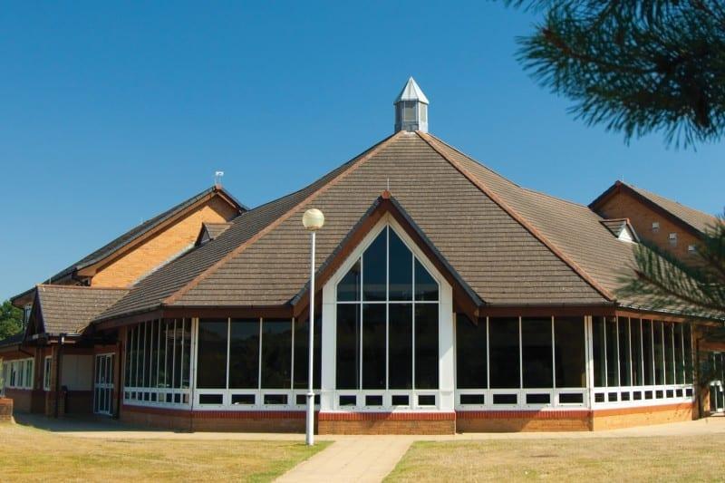 A rounded single-storey building with a path leading towards and around it. A lawn is either side of the path.
