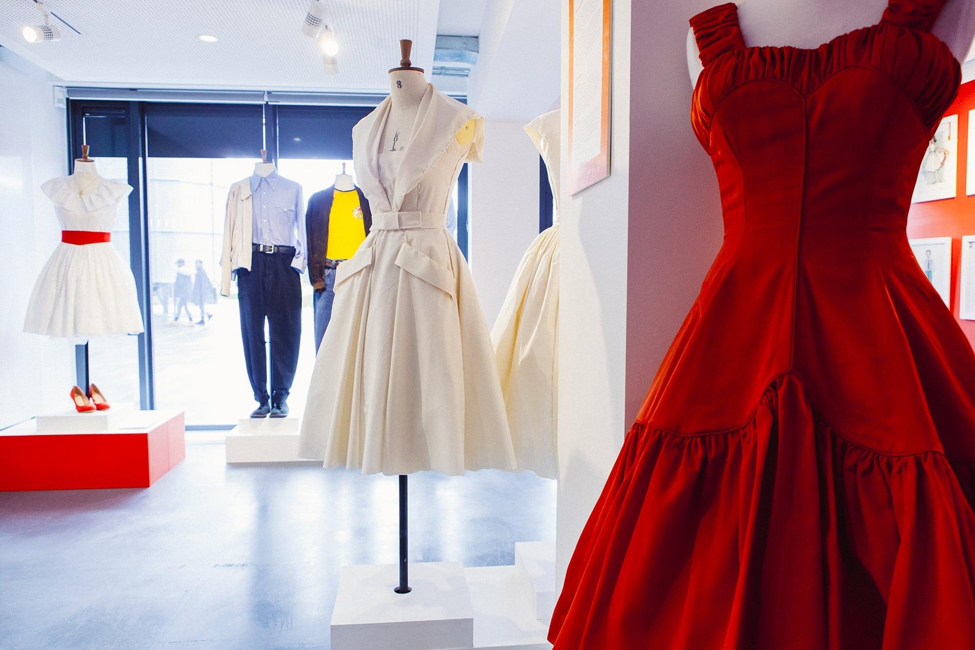 A selection of women's dresses and men's outfits on display on mannequins in a gallery.