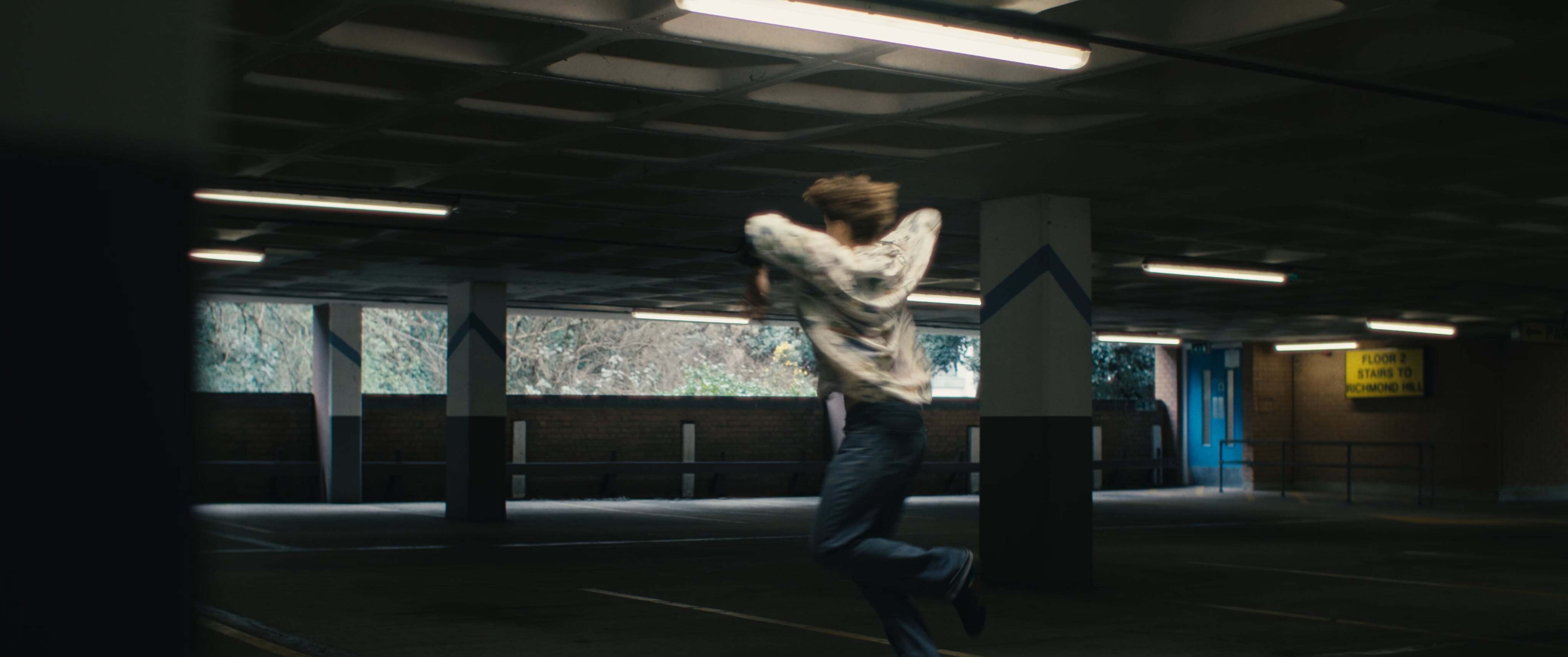 Person in white clothing mid-jump in dimly lit underground station with fluorescent lighting and tiled walls.