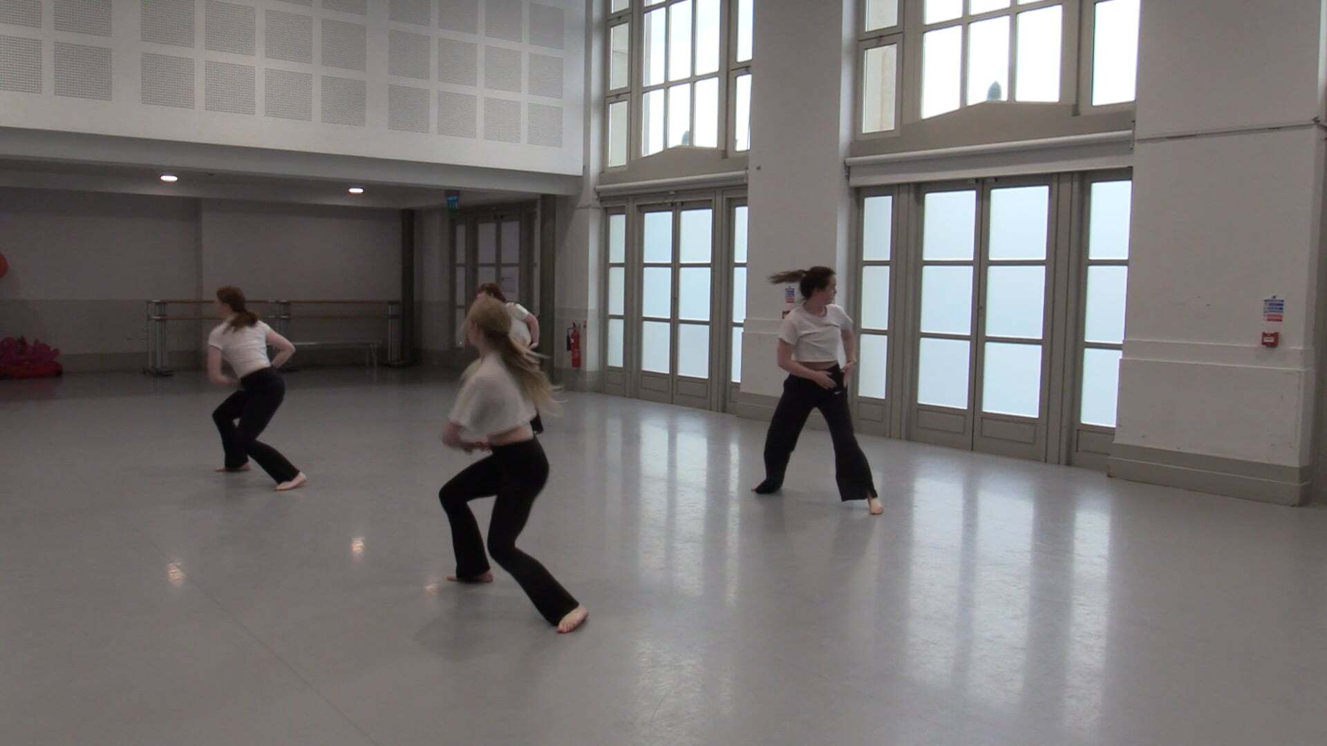 Three people dancing in a large indoor space with polished floors, tall windows, and modern architecture.