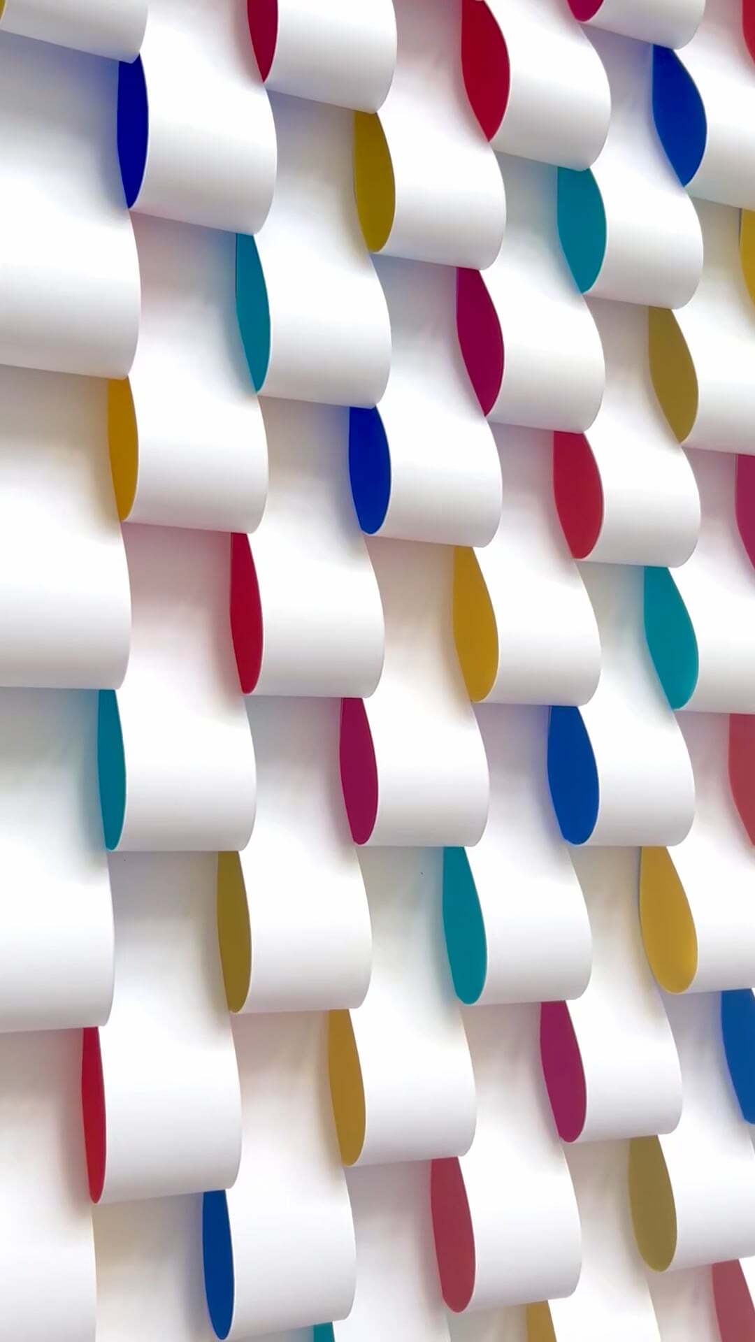 White paper chains hanging vertically with coloured inner surfaces in blue, red, yellow, teal, and pink creating a geometric pattern.
