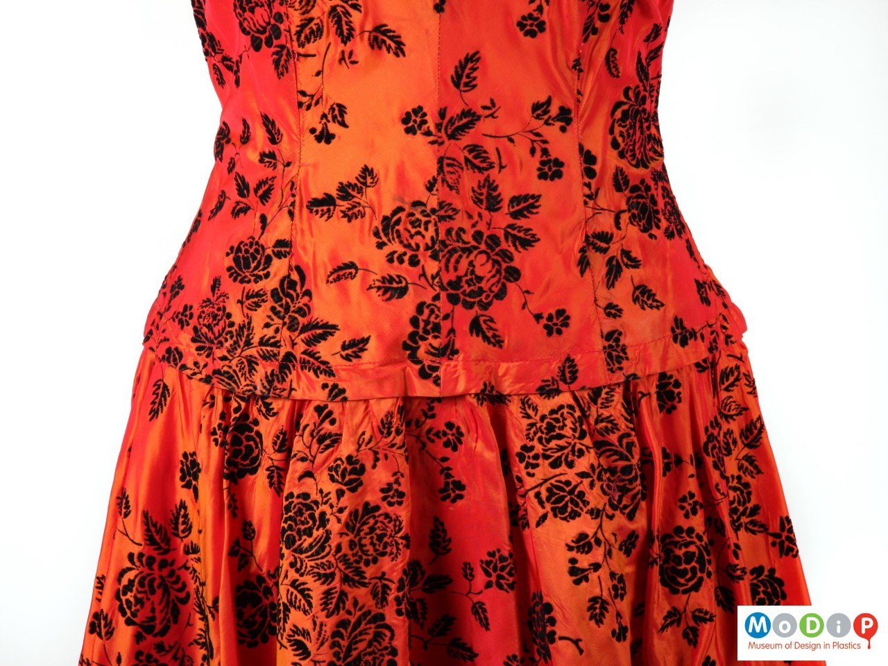 Close up of a red-orange dress with a black floral pattern.
