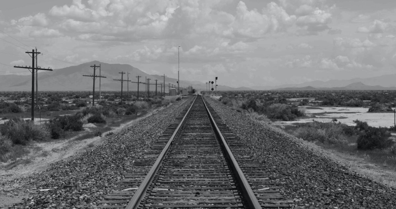 Black and white image of a railway track with a series of telephone poles running along the left-hand side.