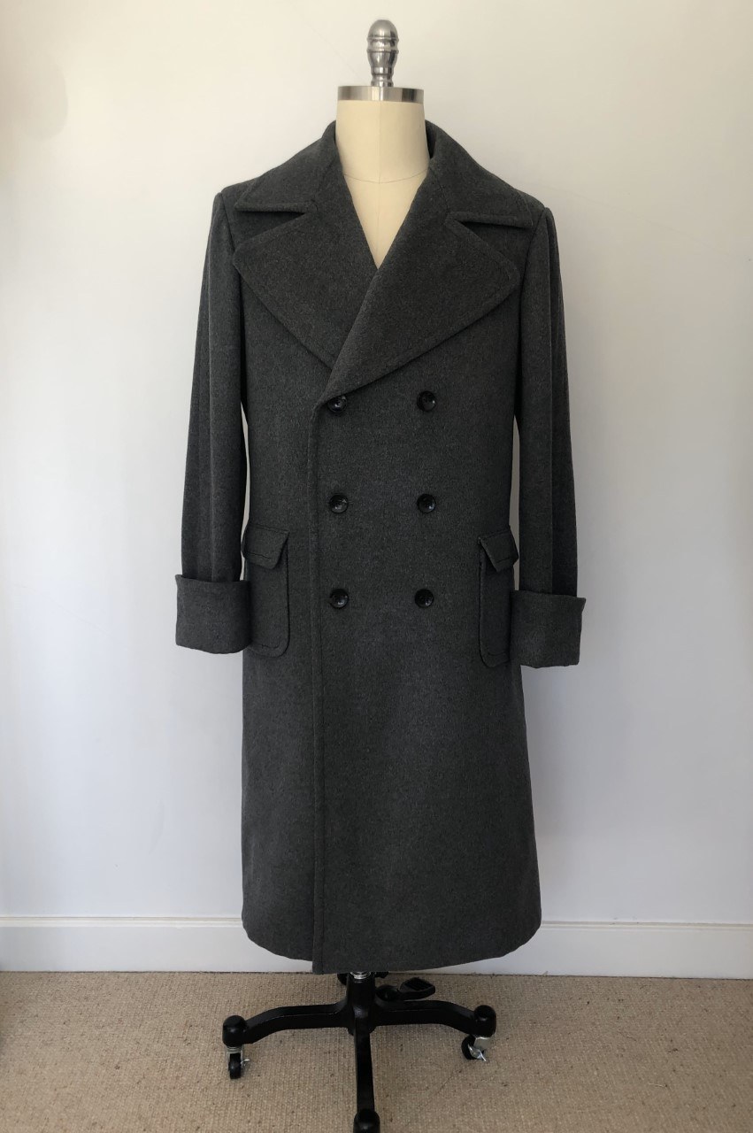 A long double-breasted coat hanging on a mannequin against a plain wall.