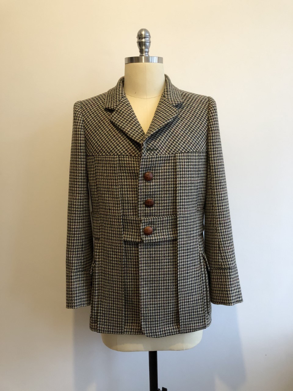 A short tweed suit jacket hangs on a mannequin against a plain wall.