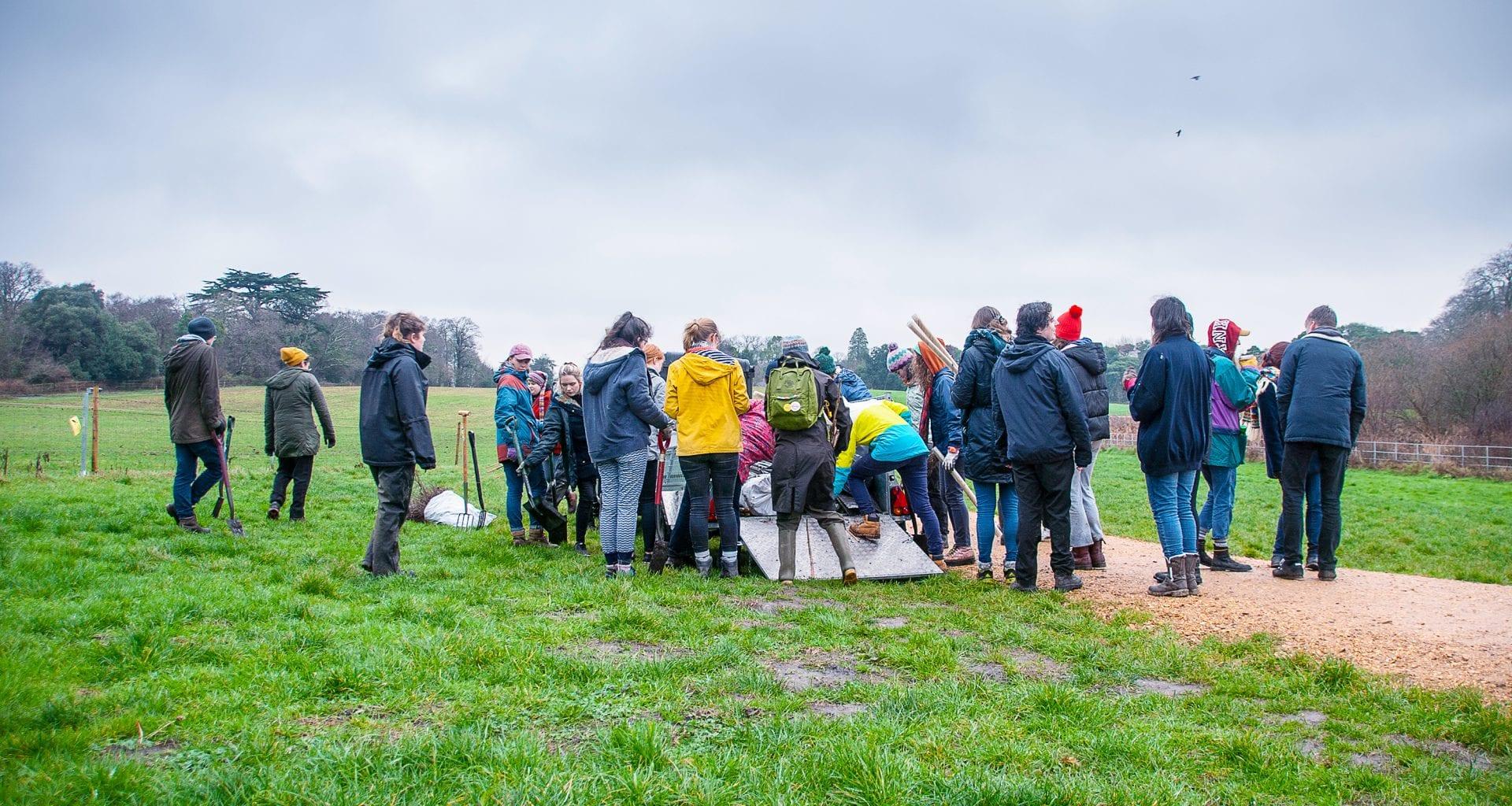 A small crowd gather outside in a field next to a footpath