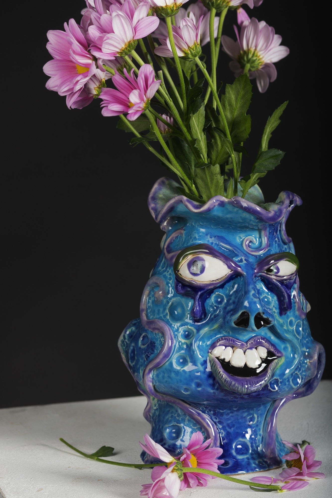 Blue ceramic vase styled into an exaggerated face with pink flowers in it.