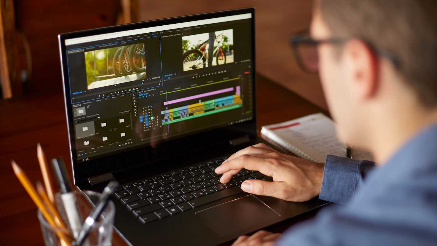 A laptop screen showing the interface of video editing software. A person sits at the laptop editing a video.