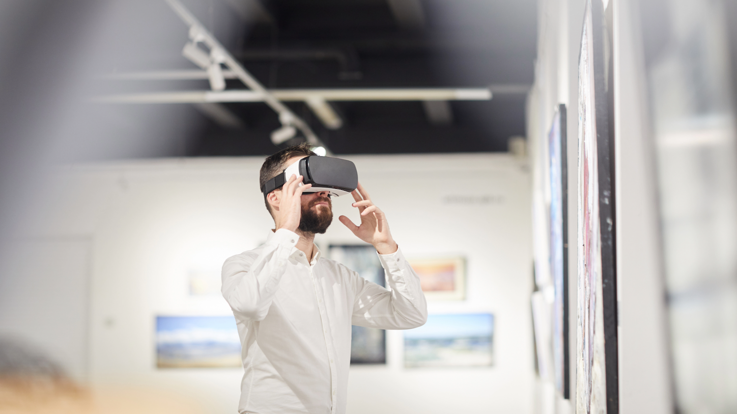 Person in white shirt standing in a gallery space wearing a VR headset over their eyes.