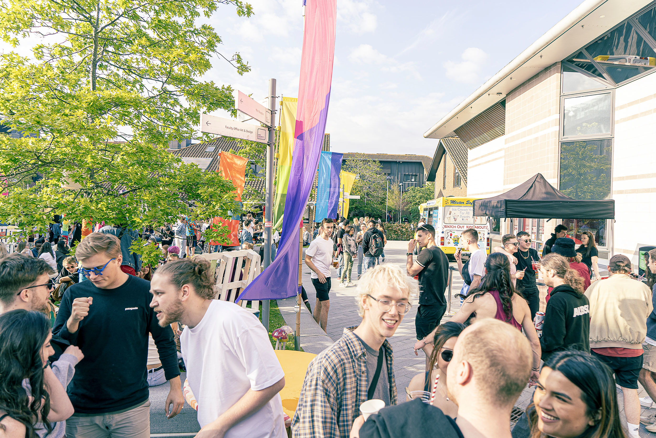 Crowds of students mingling on a university campus with banners and buildings in the background.