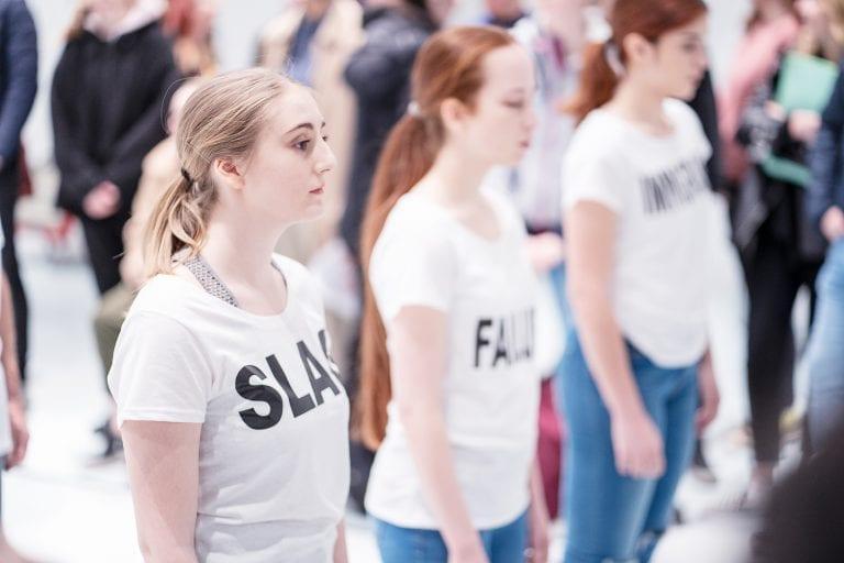 Three performers stand next to each other wearing T-shirts with words printed in bold on the front.