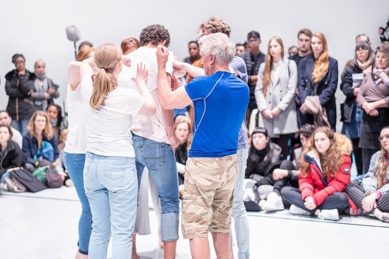 A small group of people gather around and touch another person. A crowd watches from the side.
