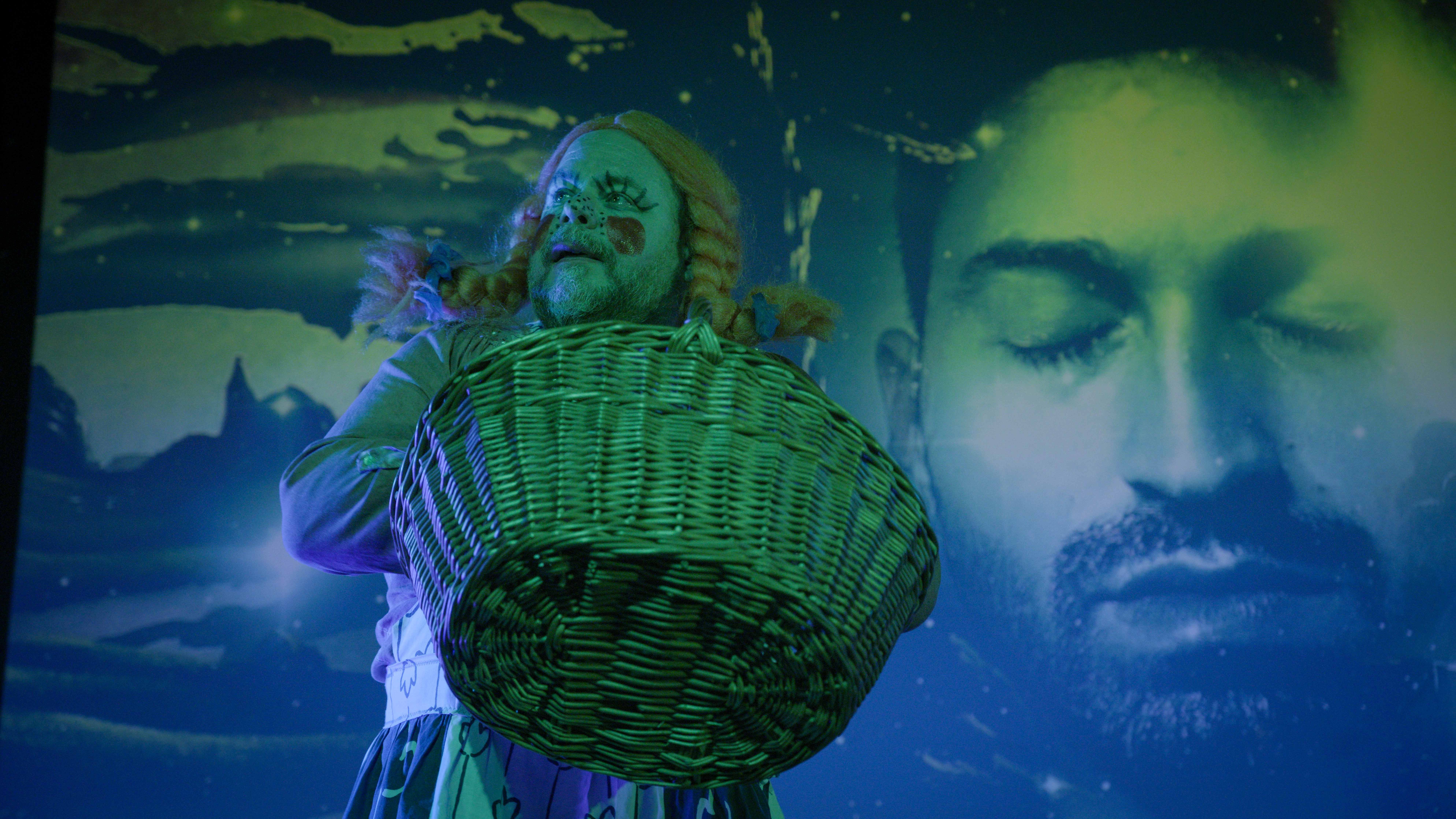 Person carrying large wicker basket on back, overlaid with blue and green tones. Blurred face visible in background.